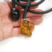 Hand holding a leather necklace with a black pendant and an amber pendant on a white background