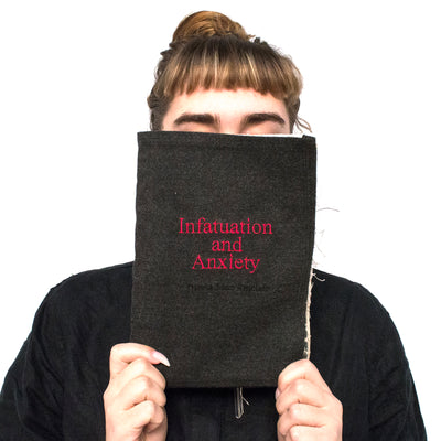 Olivia Mae Sinclair artist, holding up handmade book entitled Infatuation and anxiety